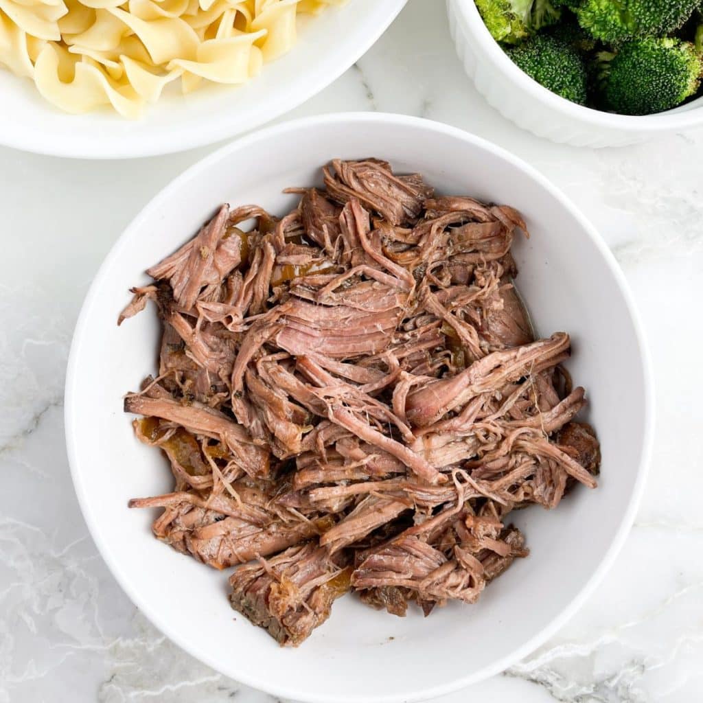 Bowl of shredded beef, bowl of noodles and broccoli.