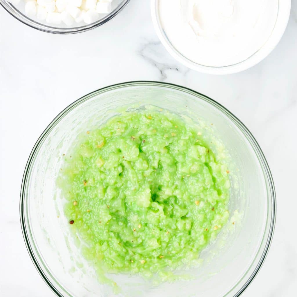 Bowl with a mixture or pineapple tidbits and pistachio pudding.