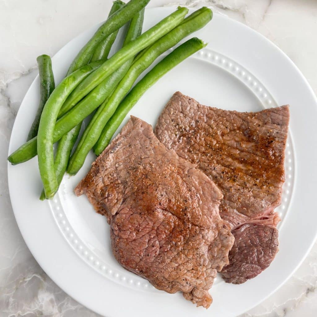 Plate with cooked steak and green beans.