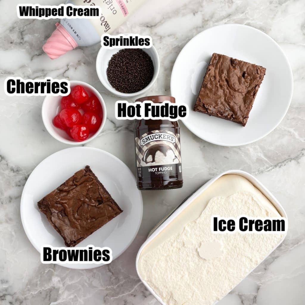 Plate with brownie, ice cream, bowl of sprinkles, and cherries. 