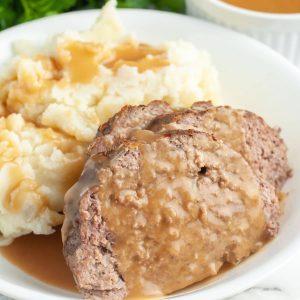 Meatloaf with gravy and mashed potatoes on a plate.