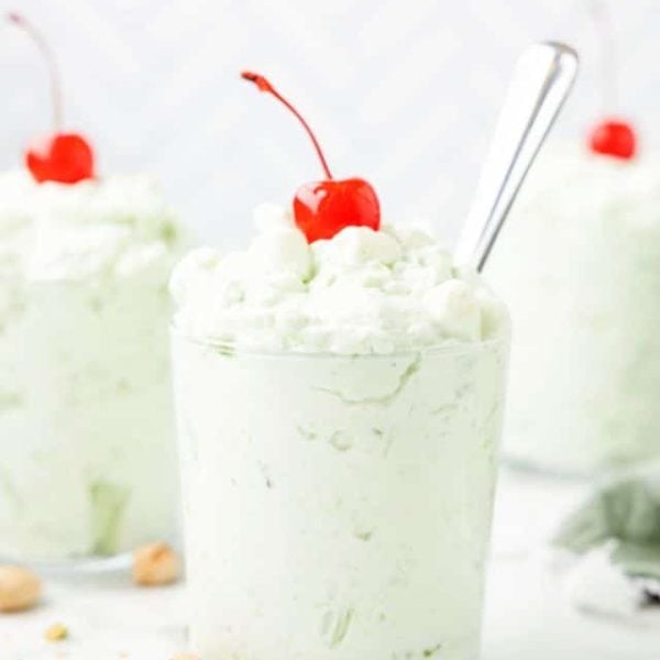 Cups filled with watergate salad topped with a cherry.