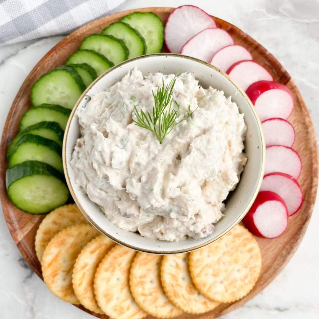 Bowl of salmon dip with sliced cucumbers, radish, and crackers. 