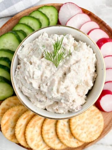 Bowl of salmon dip with sliced cucumbers, radish, and crackers.