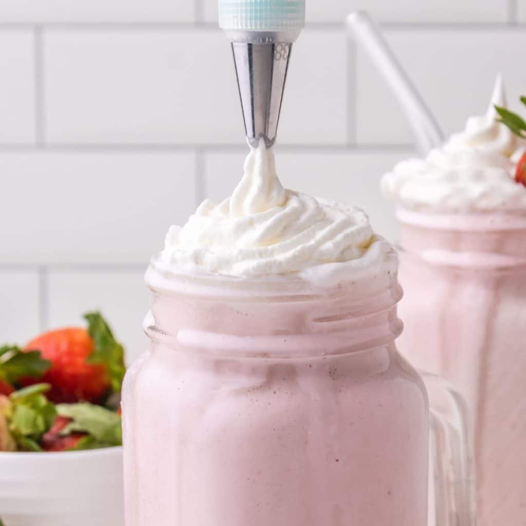 Whipped cream topping on strawberry milkshake. 