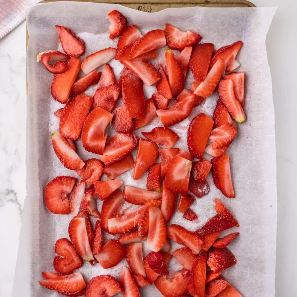 Sliced strawberries on a parchment paper lined baking sheet. 
