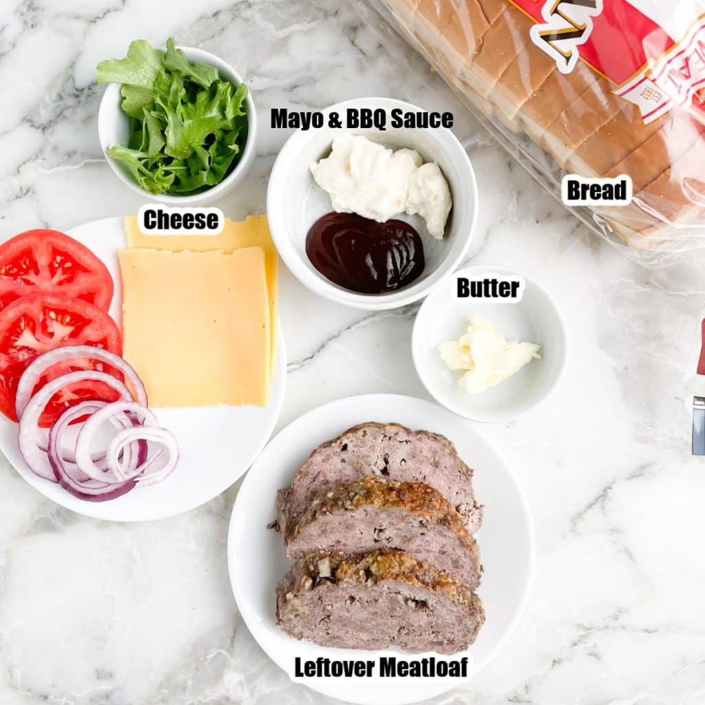 Slices of meatloaf, bread, mayonnaise, lettuce, tomato, and onion.