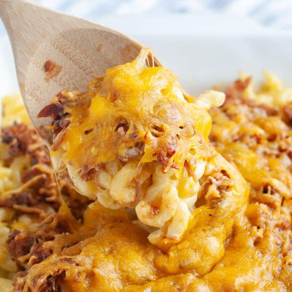 Macaroni and cheese with bbq pork on a wooden spoon.