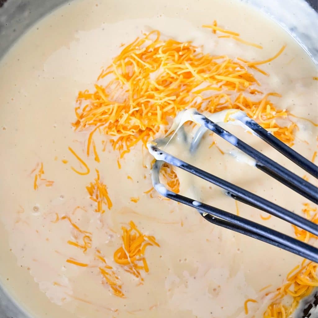Pot with melted cheese and a whisk.