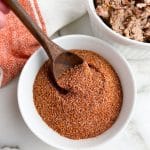 Bowl of spice mixture with a wooden spoon and bowl of pulled pork.