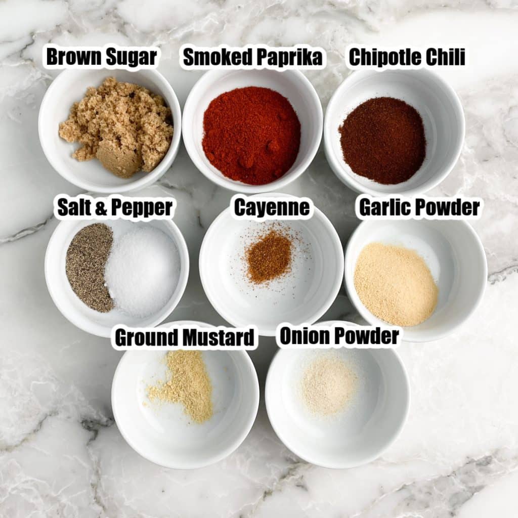 Bowls of brown sugar, paprika, chipotle chili, salt, pepper, cayenne, garlic and onion powder.