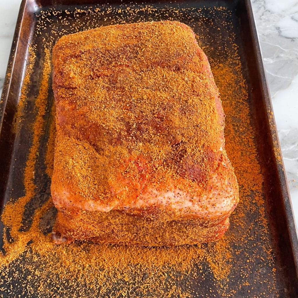 Pork roast covered in seasoning on a sheet pan. 