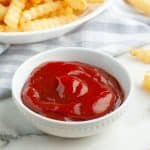Bowl of ketchup surrounded by french fries.