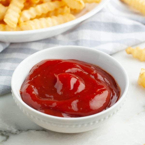 Bowl of ketchup surrounded by french fries.