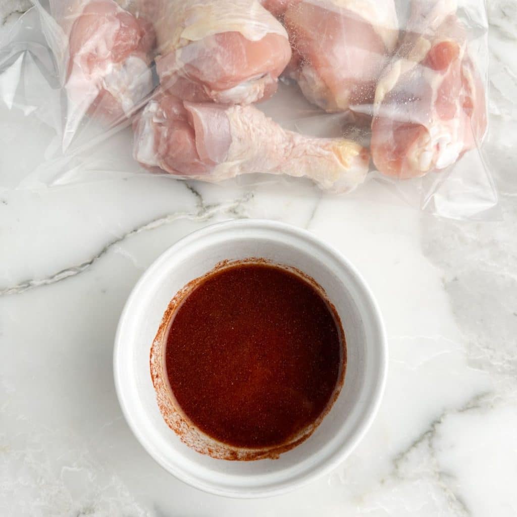 Chicken legs in a bag and bowl of seasonings. 