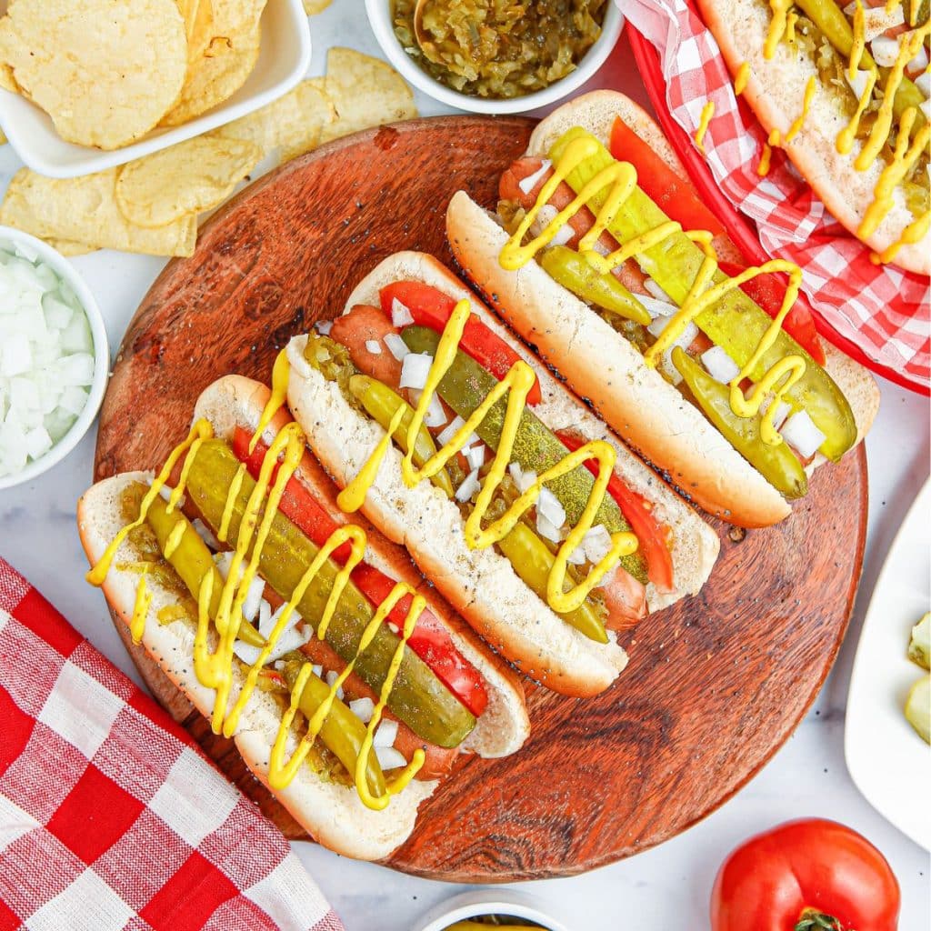 Plate of hot dogs topped with pickles and mustard. 