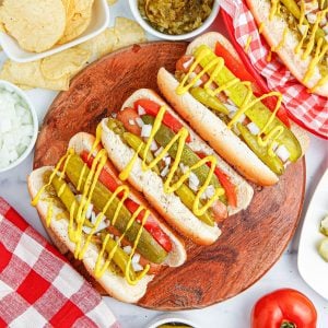 Plate of hot dogs topped with pickles and mustard.