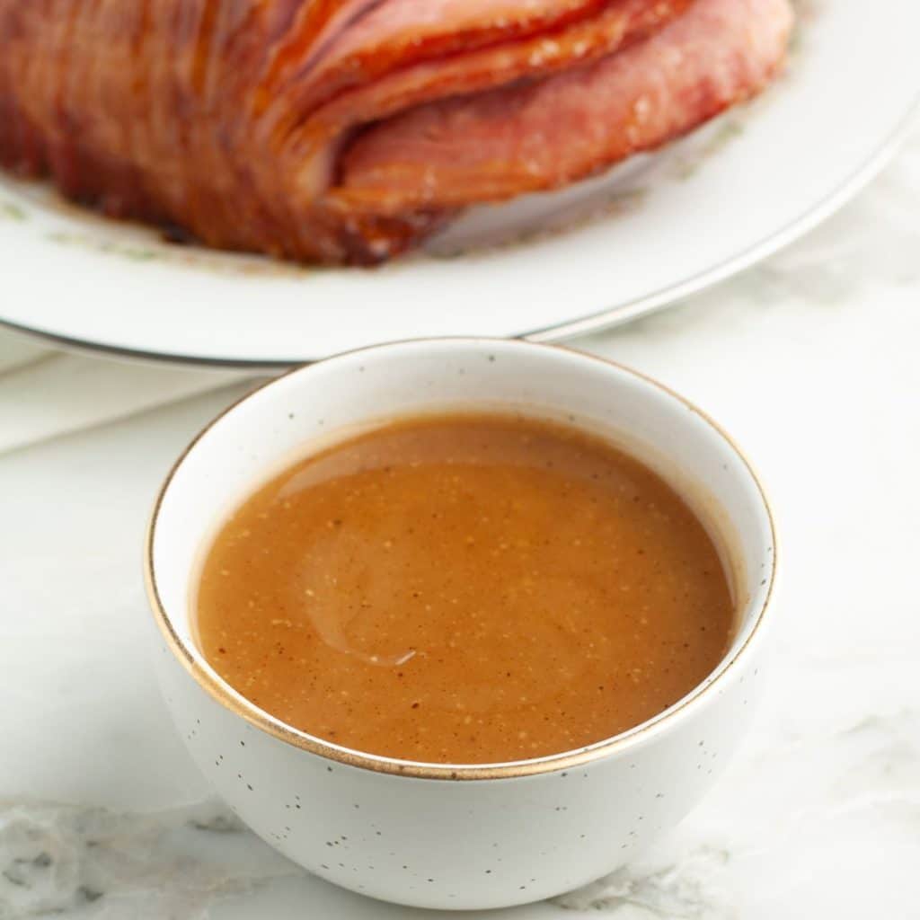 Bowl of sauce with ham in the background. 