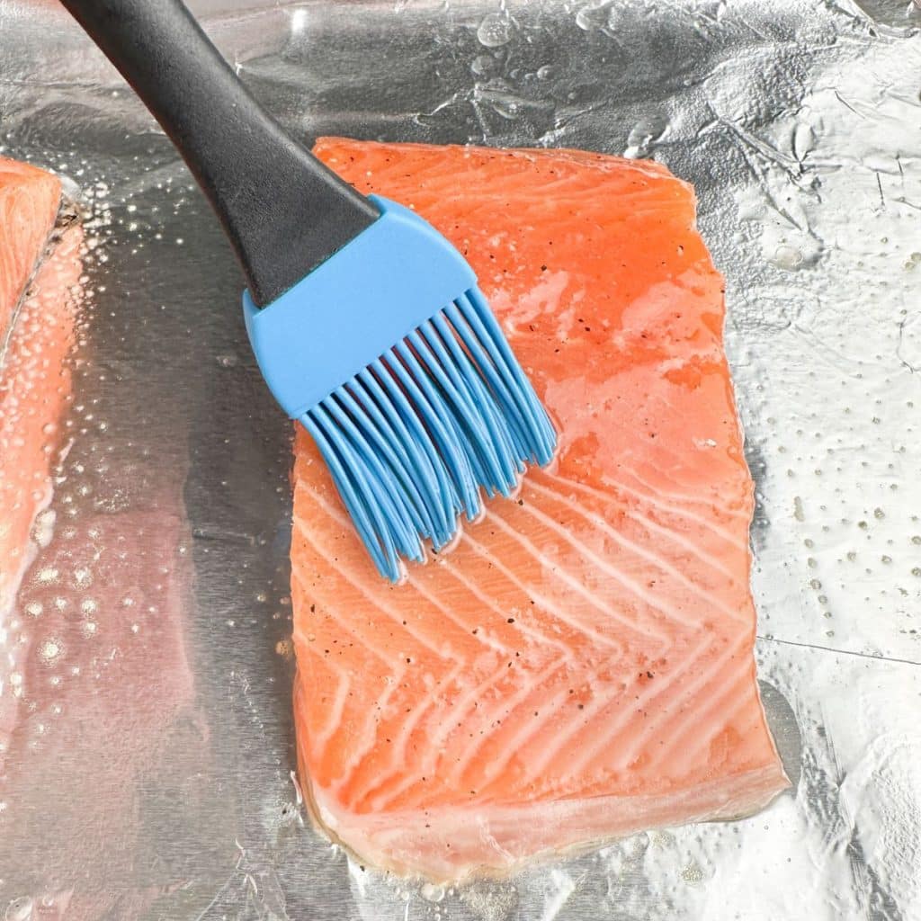 Salmon on foil with oil being brushed on top. 