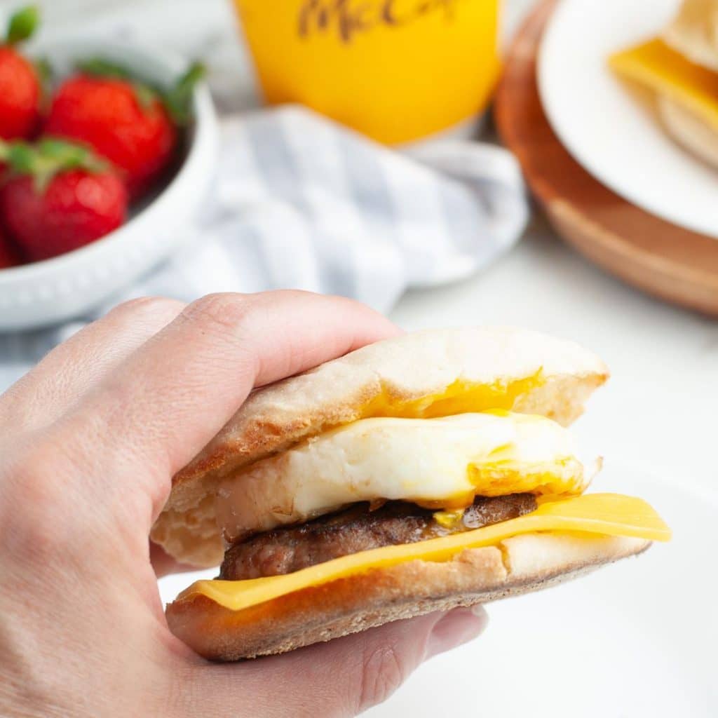 A hand holding a sausage English muffin.