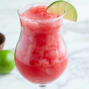 Glass with frozen watermelon margarita and a slice of lime.