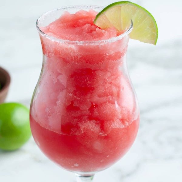 Glass with frozen watermelon margarita and a slice of lime.