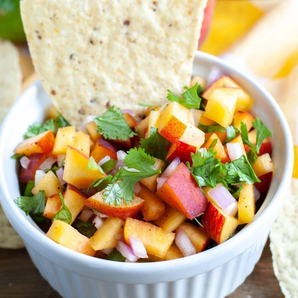 Bowl of diced peach salsa with a tortilla chip.