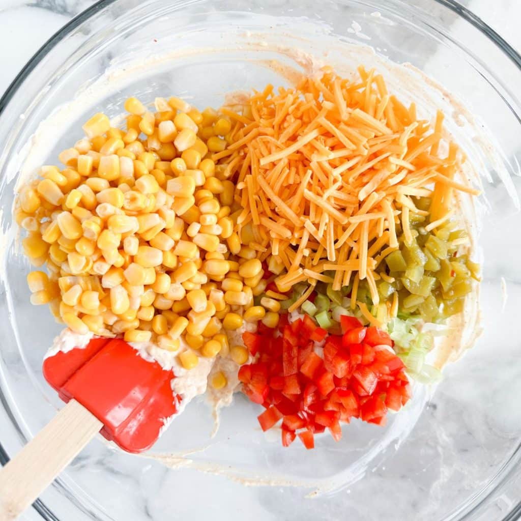 Bowl with shredded cheese, corn, diced red pepper, and green chilies. 