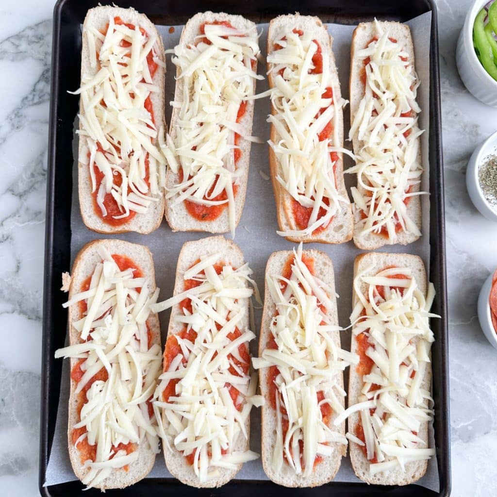 Sub rolls on pan with pizza sauce and cheese.