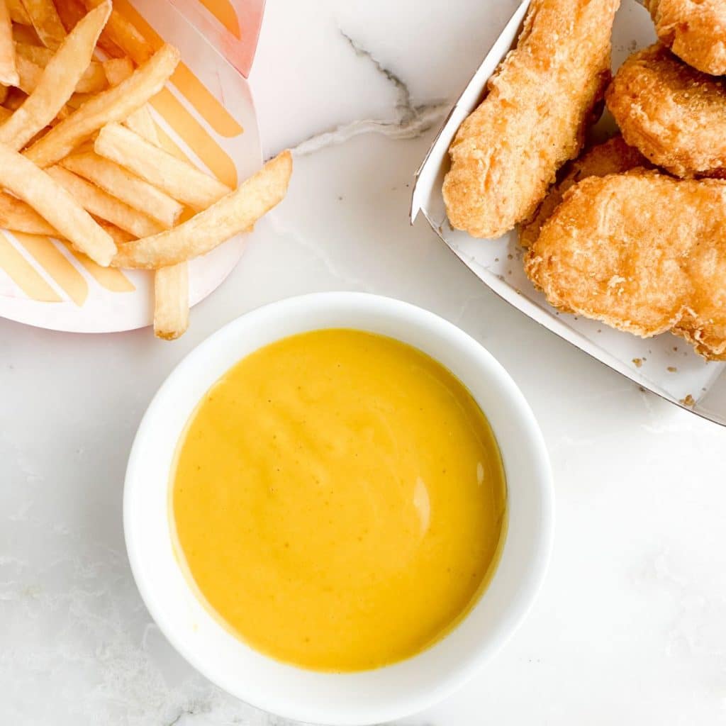 Bowl of mustard sauce, french fries and chicken nuggets. 