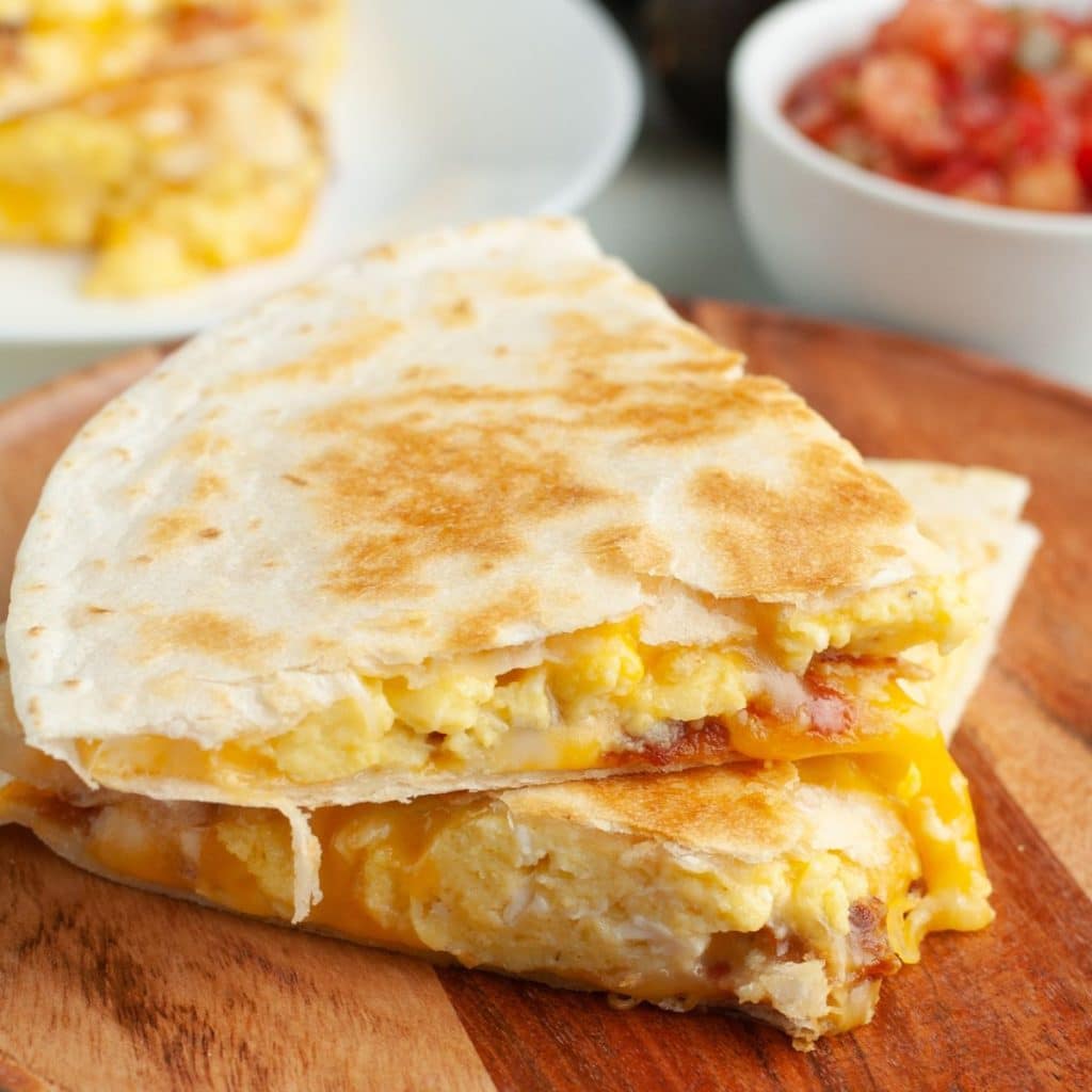 Breakfast quesadilla stacked on wooden plate. 