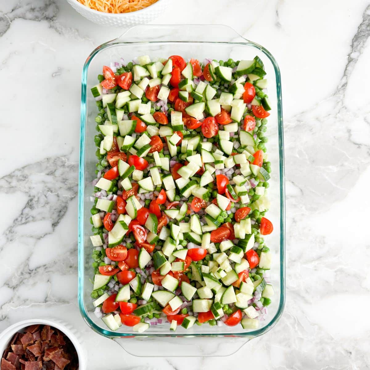 Casserole dish with peas, onions, cucumbers, and tomatoes. 