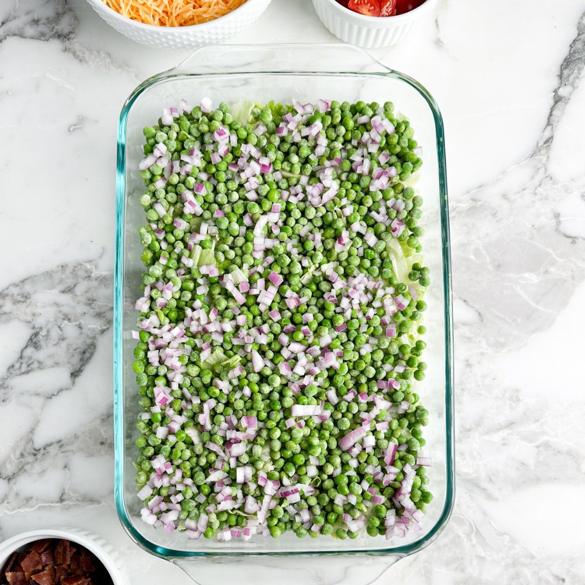 Casserole dish with lettuce, peas, and onions. 