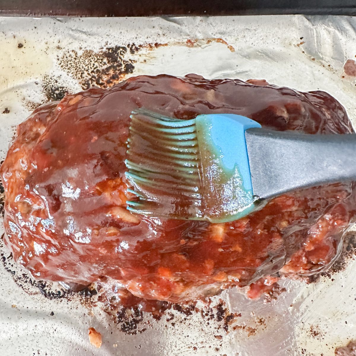 BBQ sauce being brushed on meatloaf. 
