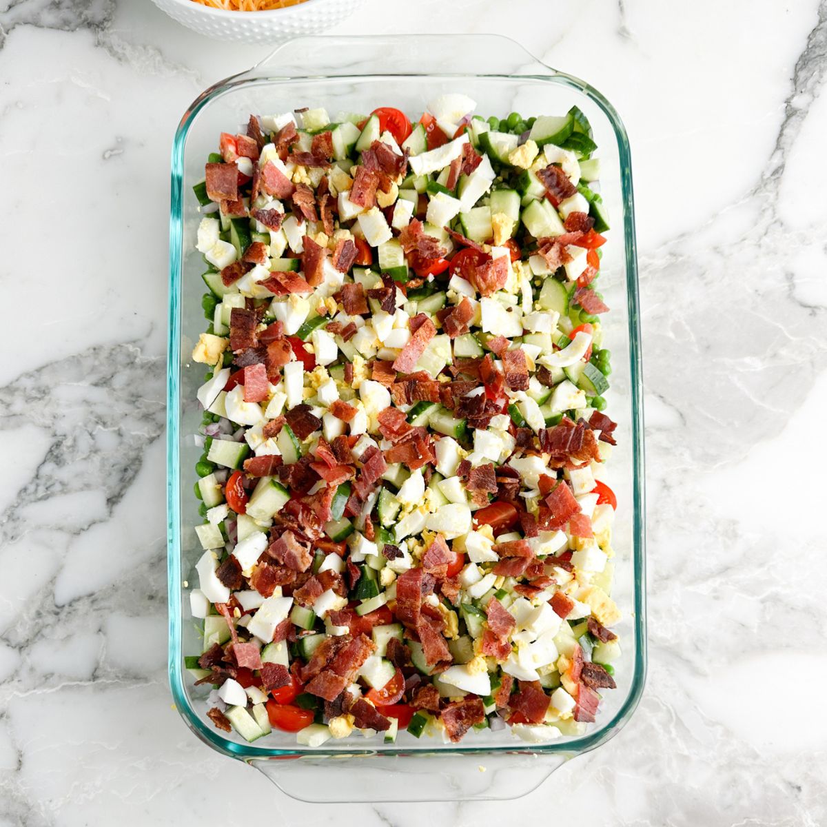 Casserole dish with chopped egg, bacon, lettuce. 