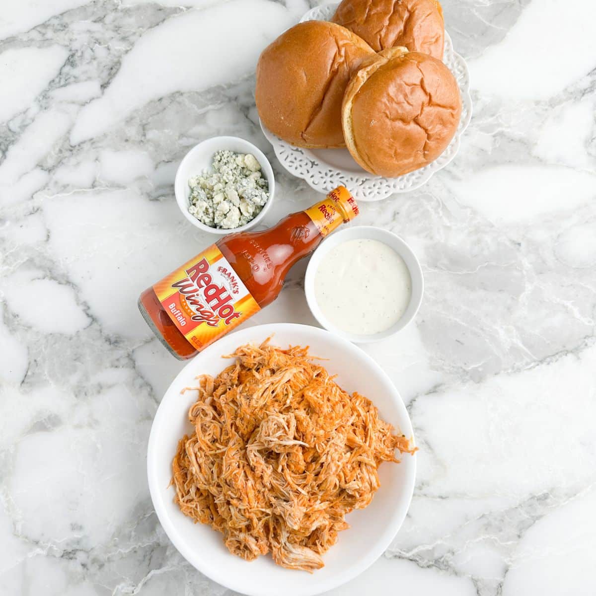 Buns, shredded chicken, bottle of buffalo sauce. 