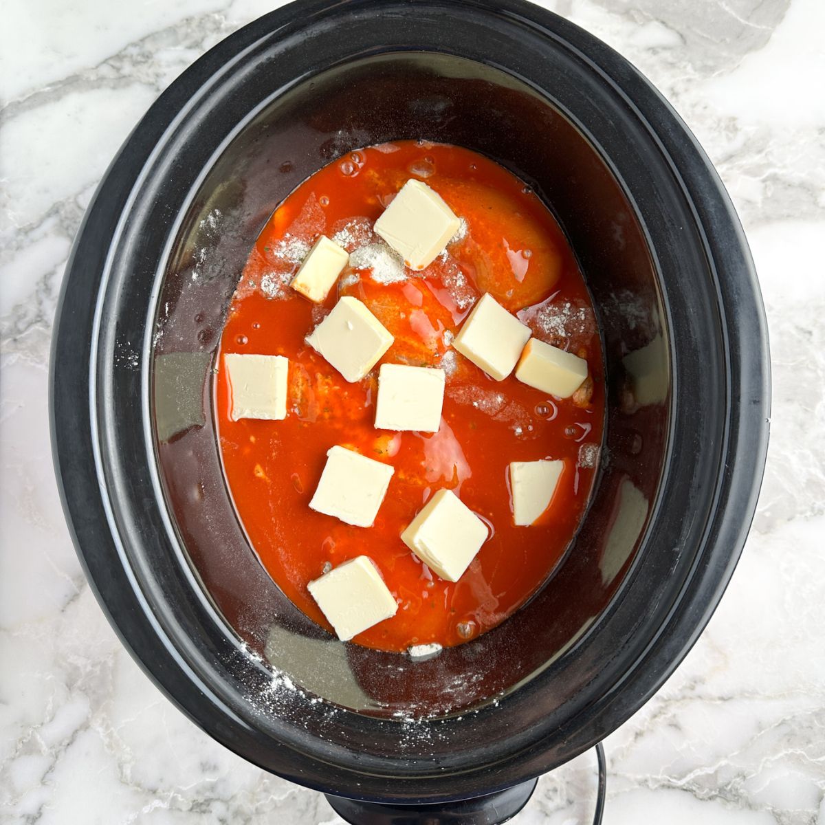 Slow cooker with chicken, hot sauce, and butter.