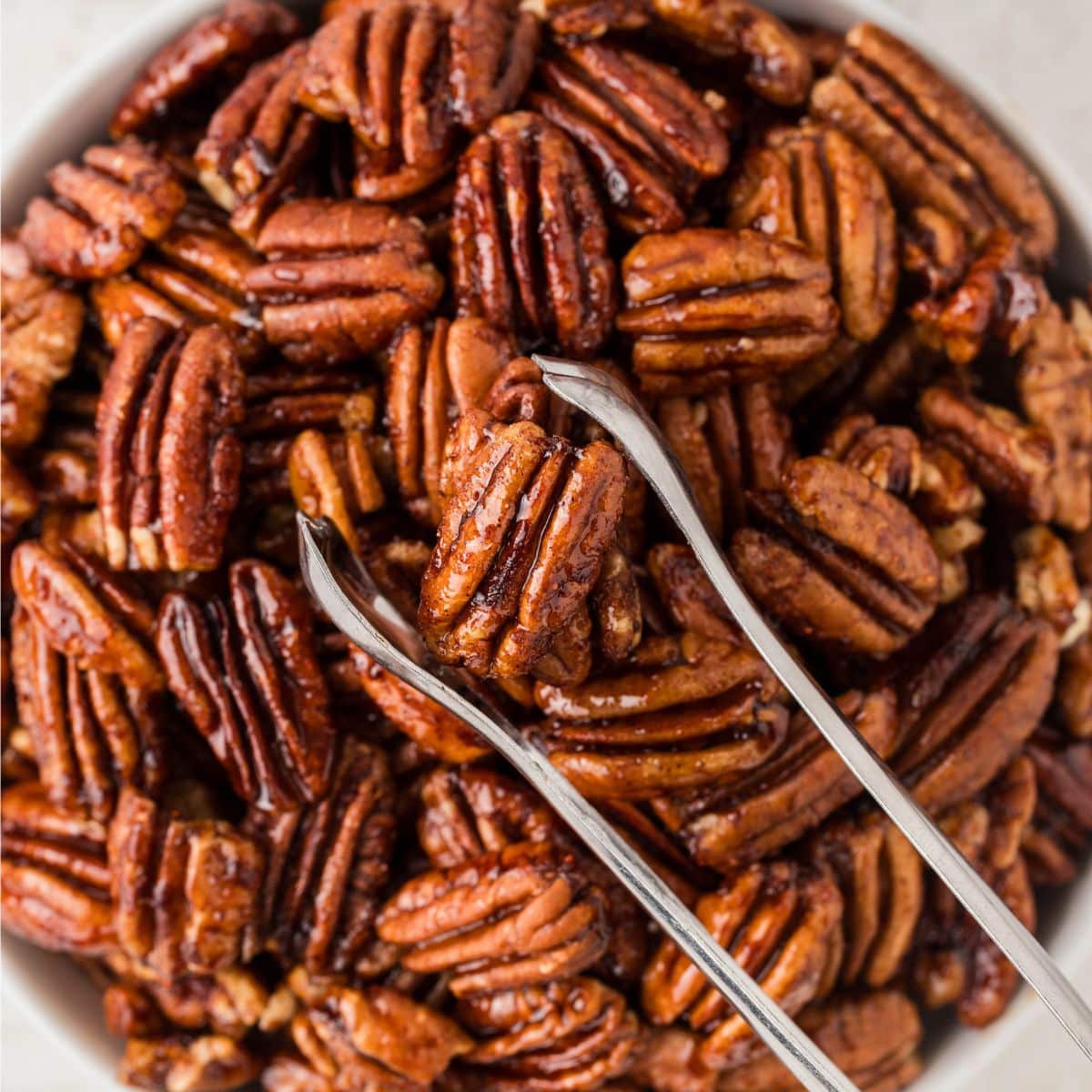 Bowl of pecans with tongs.