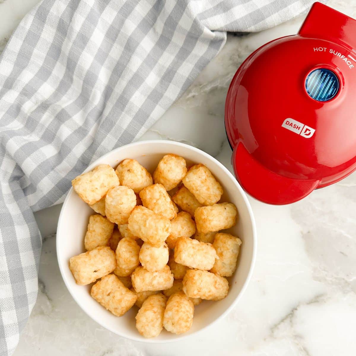 Bowl of tater tots and red mini waffle maker. 