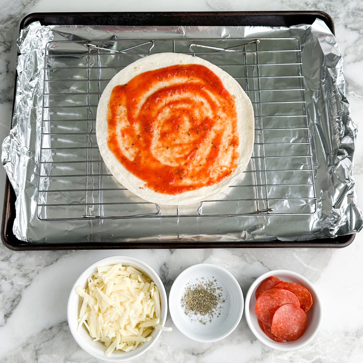 Tortilla on a rack topped with pizza sauce. 