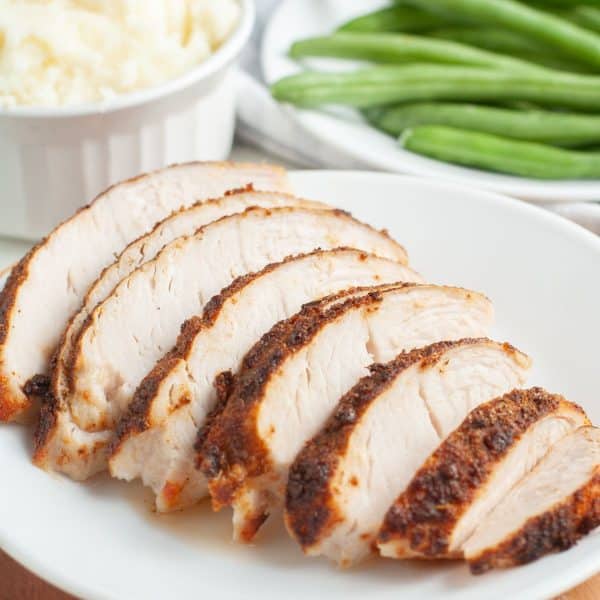 Sliced turkey tenderloin on a plate with beans and mashed potatoes.