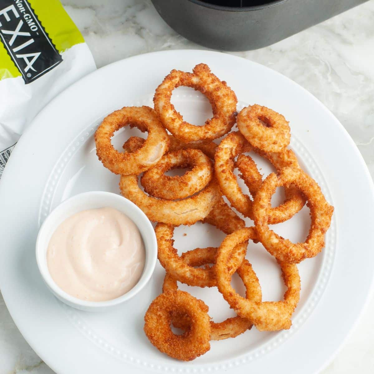 Plate of onion rings with a bowl of creamy sauce. 