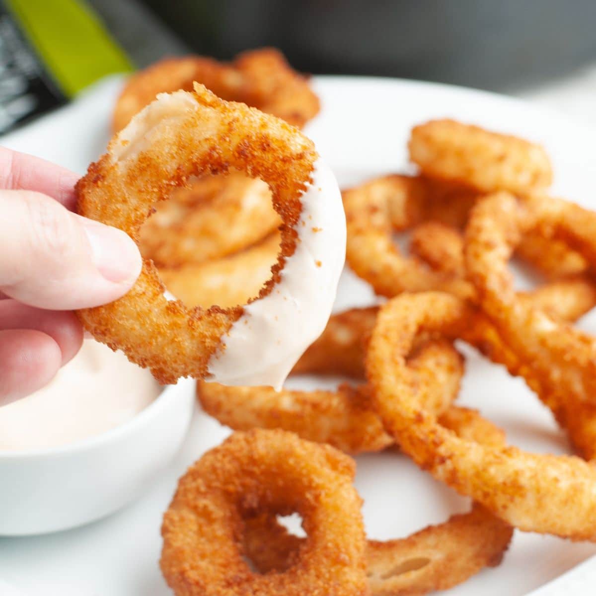 Hand holding an onion ring with sauce. 