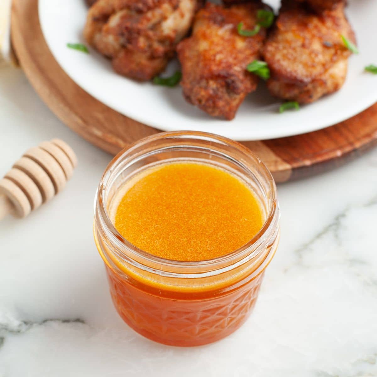 Jar of hot honey wing sauce with a plate of wings. 