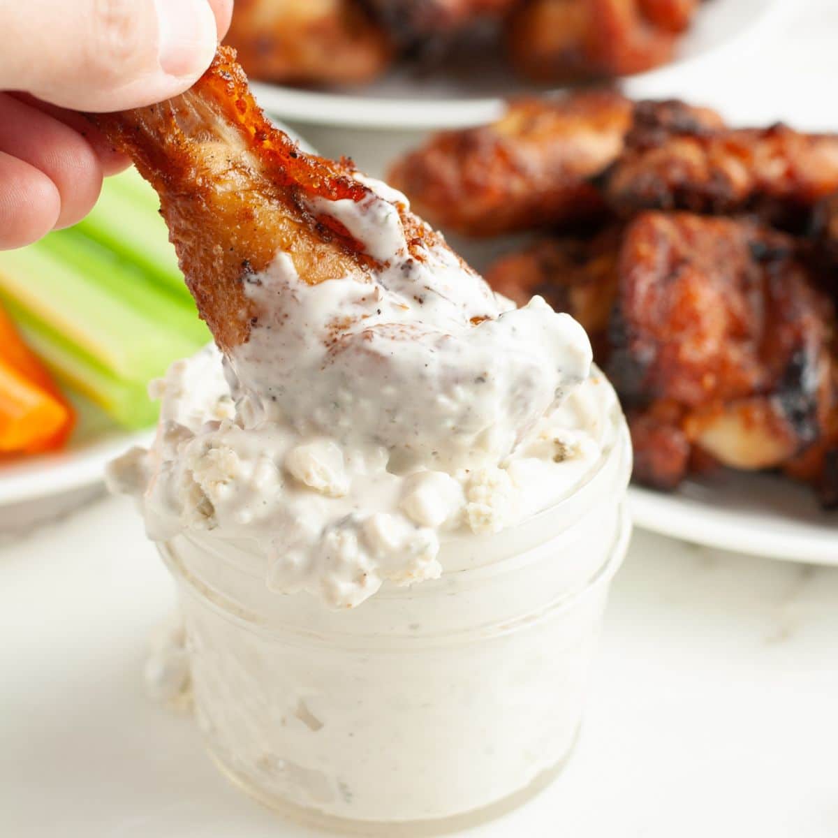 Jar with blue cheese sauce and chicken wing being dipped. 