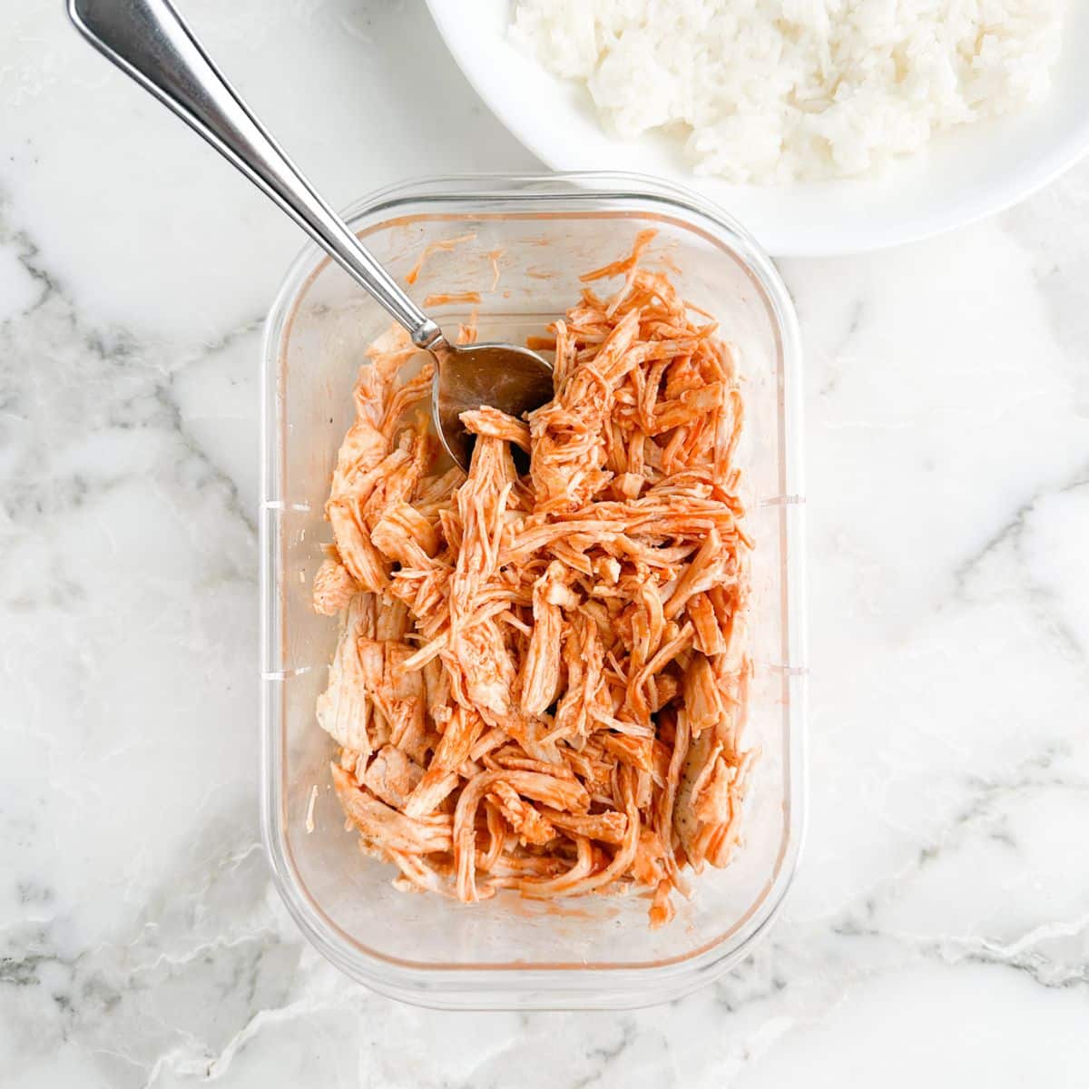 Shredded chicken in a container with buffalo sauce and a spoon. 
