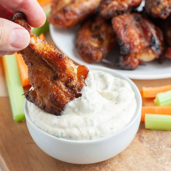 Chicken wing dipping into creamy sauce.