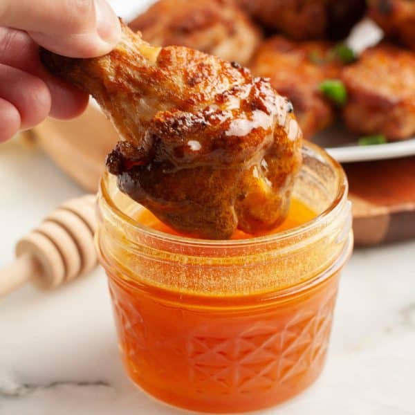 Chicken wing dipping into honey wing sauce.