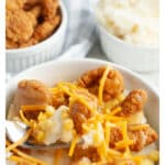 Bowl of chicken nuggets with mashed potatoes and cheese.