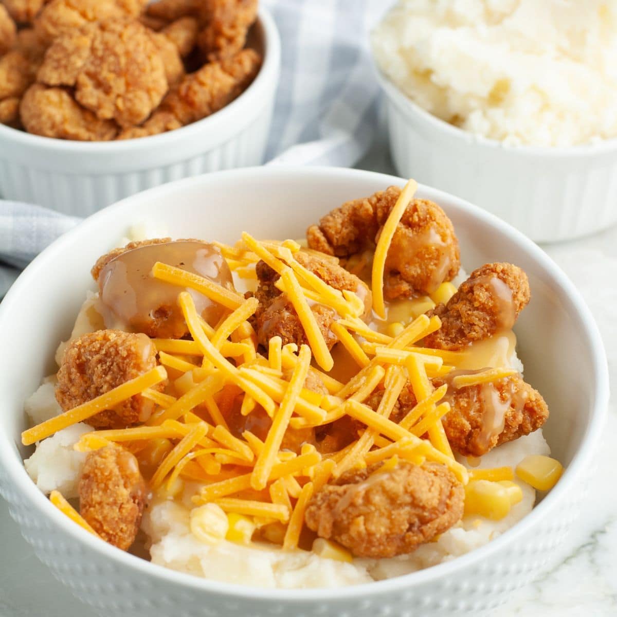 Bowl filled with mashed potatoes, popcorn chicken, and shredded cheese. 